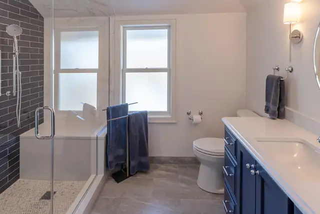 Bathroom with navy vanity, white quartz top and a glass shower with dark subway tile