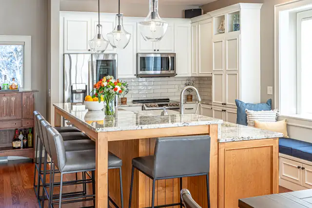 Kitchen with white cabinets, a maple island with a granite top, gray counter stools and glass globe pendants