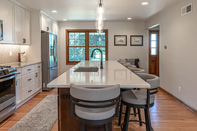 Kitchen remodel with a long white quartz island, gray bar stools, white cabinets and wood floors