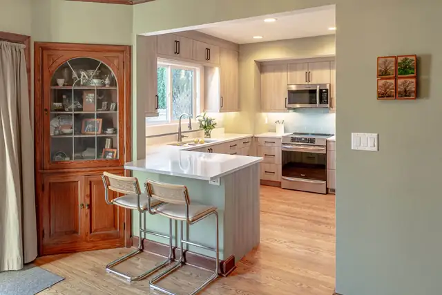 Kitchen remodel with light wood-grain slab cabinets, quartz peninsula seating and blue glass backsplash