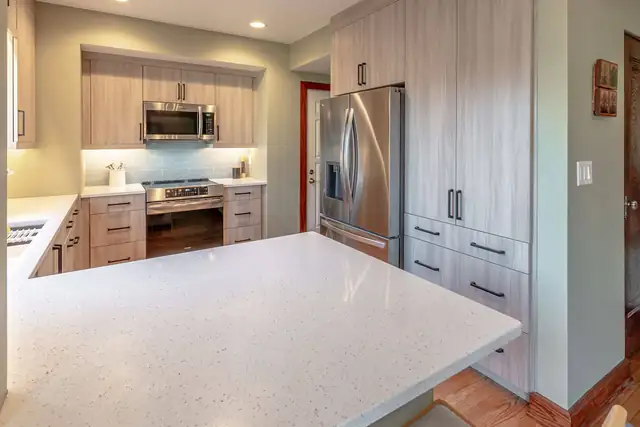 Kitchen with stainless range and microwave, under-cabinet lighting, blue glass tile and tall pantry cabinets