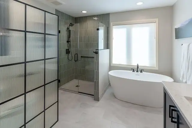 Primary bathroom remodel with a freestanding tub, sage green tile shower and black grid fluted glass partition