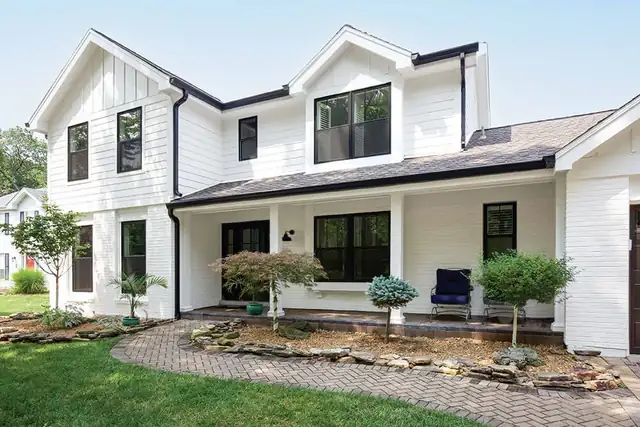 White farmhouse with black Infinity by Marvin replacement windows, covered porch and stone walkway