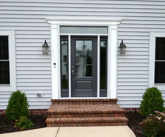 Charcoal ProVia entry door with glass sidelites and white trim on a gray-sided home with brick steps