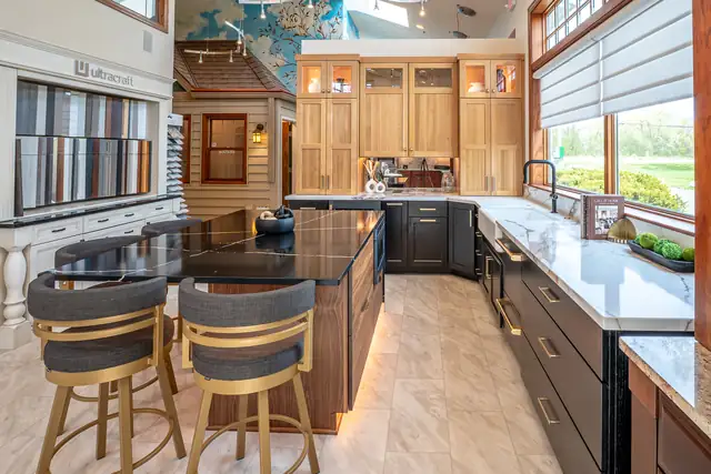Kitchen display at the Callen Design Center with natural maple cabinets, a dark island with brass stools and marble-look counters